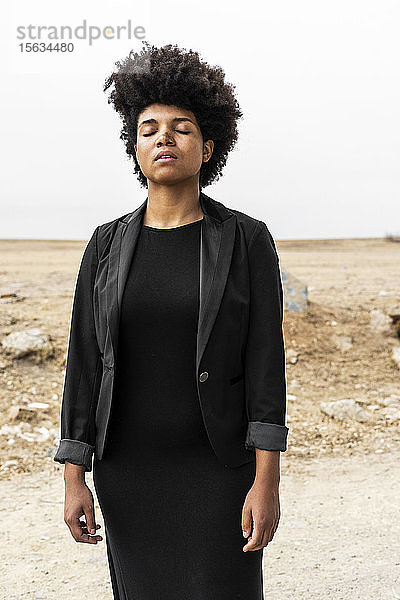 Porträt einer in Schwarz gekleideten jungen Frau in trostloser Landschaft stehend
