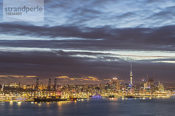 Beleuchtete moderne Gebäude am Meer gegen bewölkten Himmel in der Abenddämmerung in Auckland  Neuseeland