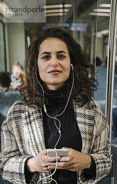 Porträt einer schönen jungen Frau mit Kopfhörern und Smartphone in der U-Bahn