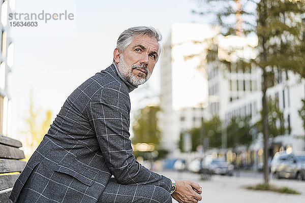Porträt eines modisch reifen Geschäftsmannes  der auf einer Bank in der Stadt sitzt