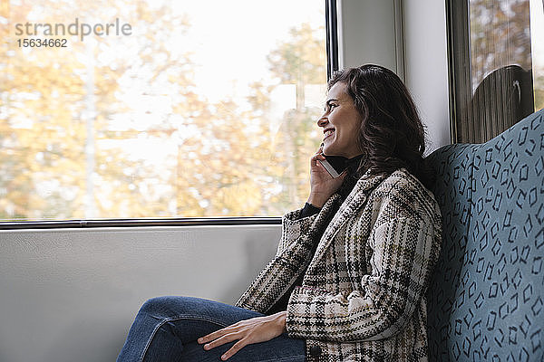 Lächelnde junge Frau am Telefon in der U-Bahn