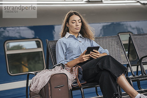 Junge weibliche Reisende wartet am Bahnhof und benutzt E-Book
