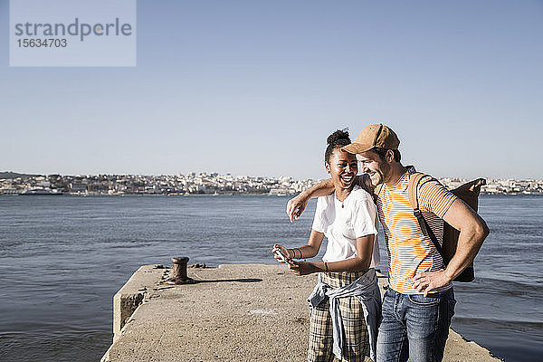 Glückliches junges Paar telefoniert am Pier am Wasser  Lissabon  Portugal
