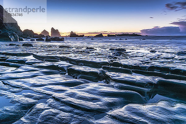 Neuseeland  Südinsel  felsige Meeresküste in der Abenddämmerung mit Motukiekie Beach-Meeresschornsteinen in der Ferne
