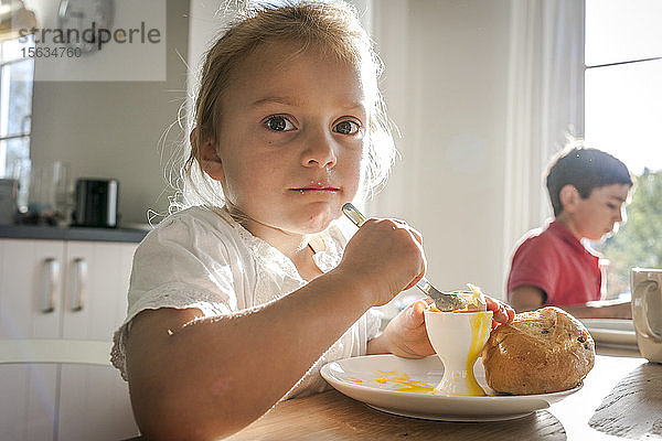 Porträt eines Mädchens  das am Esstisch ein gekochtes Ei isst