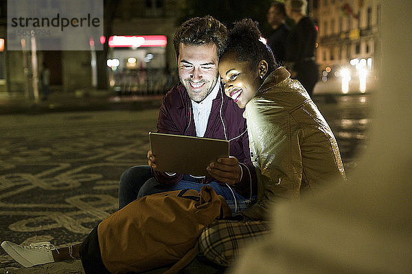 Porträt eines glücklichen jungen Paares  das sich Kopfhörer teilt und dabei ein digitales Tablet betrachtet  Lissabon  Portugal