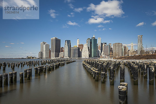 Holzpfosten im East River mit modernen Gebäuden im Hintergrund vor dem Himmel  New York City  USA