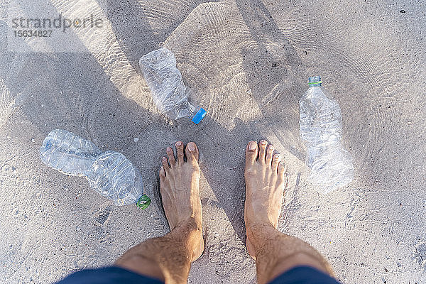 Männerfüße am Strand  umgeben von leeren Plastikflaschen  Draufsicht