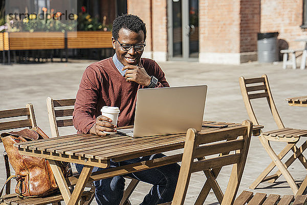 Junger Mann benutzt Laptop in einem Café und trinkt Kaffee
