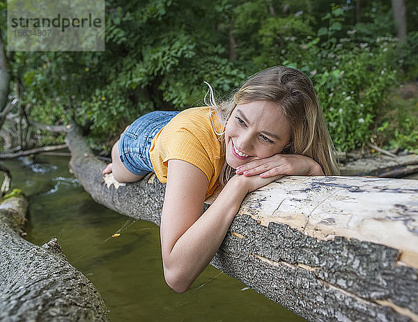 Lächelnde Frau liegt auf einem Baumstamm am Seeufer