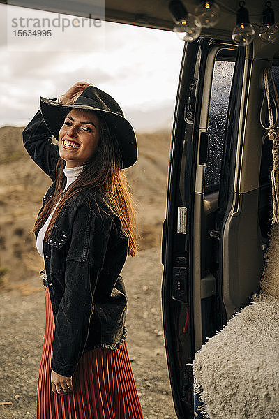 Porträt einer lächelnden jungen Frau in Wüstenlandschaft  die neben einem Wohnmobil steht  Almeria  Andalusien  Spanien