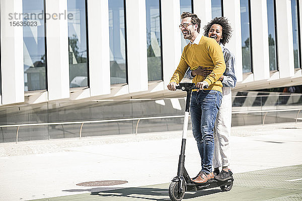 Glückliches junges Paar fährt E-Scooter in der Stadt