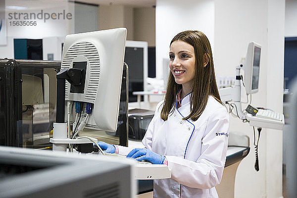 Junge Frau in weißer Kleidung benutzt Probenanalysegerät bei der Arbeit im Forschungslabor