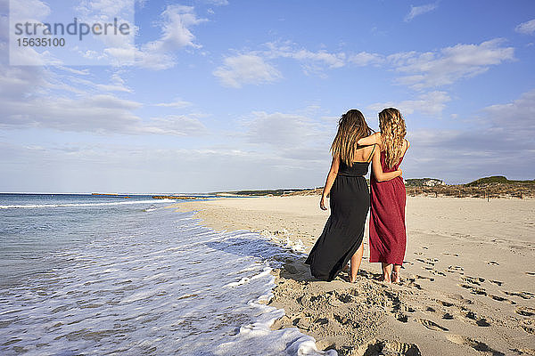 Zwei junge Frauen stehen Arm in Arm am Strand