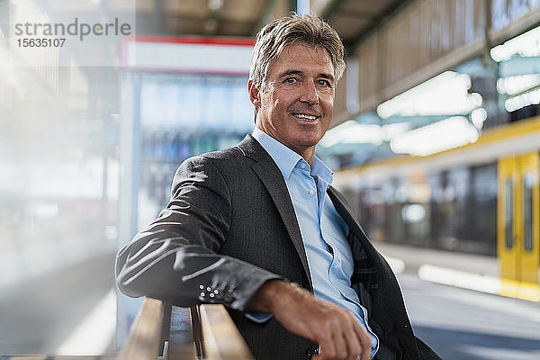 Porträt eines lächelnden reifen Geschäftsmannes  der am Bahnsteig wartet