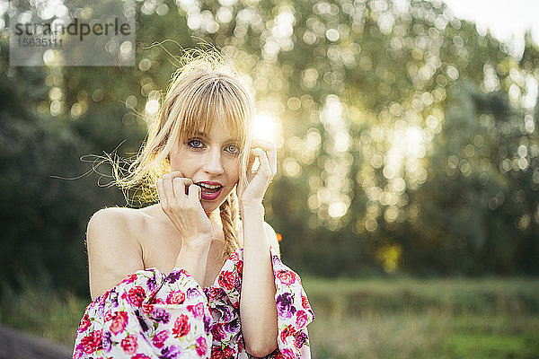 Porträt einer blonden jungen Frau in Sommerkleid mit Blumenmuster im Gegenlicht