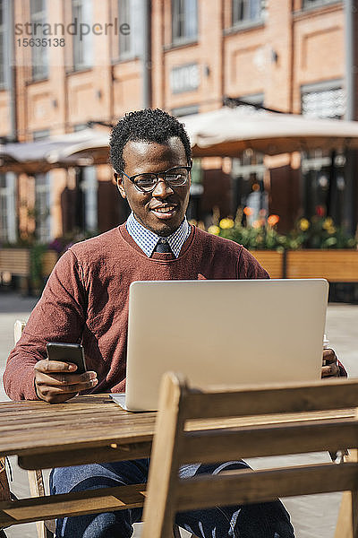 Junger Mann benutzt Smartphone und Laptop in einem Café