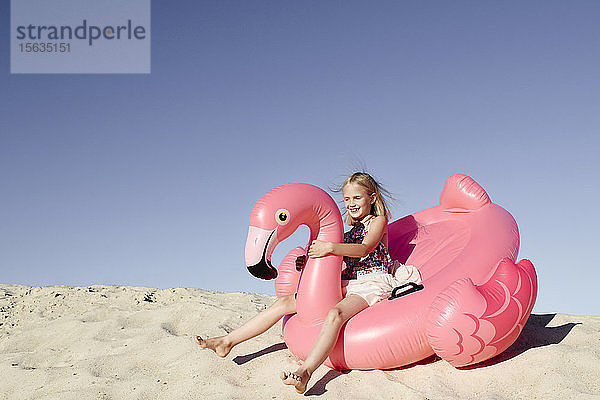 Lächelndes kleines Mädchen mit Flamingo-Pool schwimmt auf dem Sand