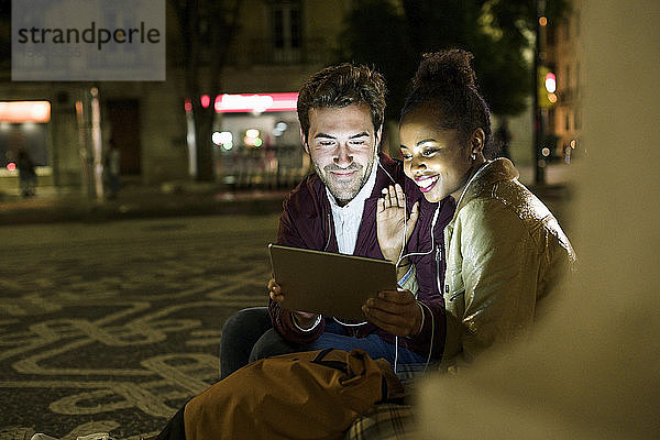 Porträt eines lächelnden jungen Paares  das sich Kopfhörer teilt  während es auf ein digitales Tablet schaut  Lissabon  Portugal
