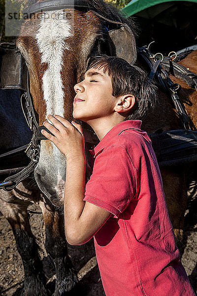 Junge mit geschlossenen Augen  der ein Pferd umarmt