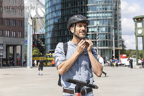 Mann befestigt den Helm  bevor er auf einem Elektroroller fährt  Berlin  Deutschland