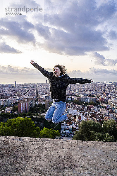 Unbeschwerte junge Frau springt bei Sonnenaufgang über die Stadt  Barcelona  Spanien