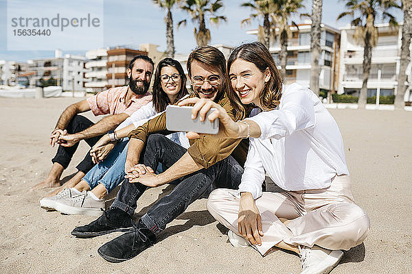 Glückliche Freunde sitzen am Strand und machen ein Selfie