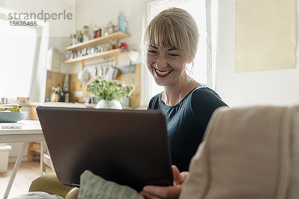Porträt einer glücklichen Frau  die mit einem Laptop in der Küche sitzt