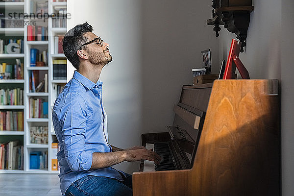 Lächelnder junger Mann mit geschlossenen Augen spielt zu Hause Klavier