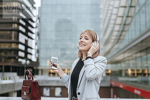 Glückliche Frau  die in der Stadt mit Kopfhörern Musik hört