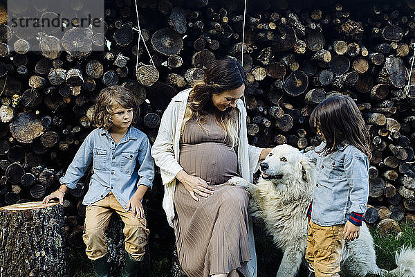 Schwangere Mutter mit zwei Kindern und Hund beim Entspannen am Holzstapel