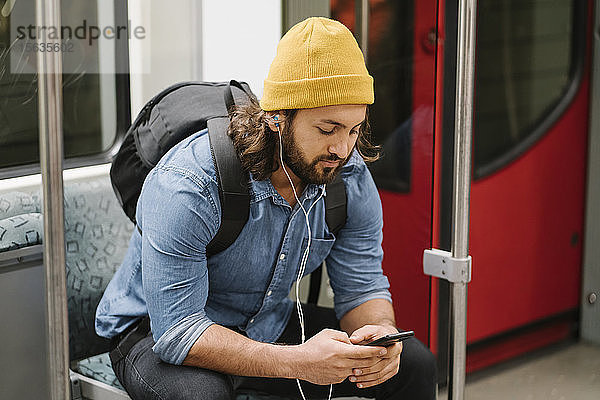 Mann mit Rucksack beim Musikhören mit Smartphone und Kopfhörern in Pendlerlinie  Berlin  Deutschland