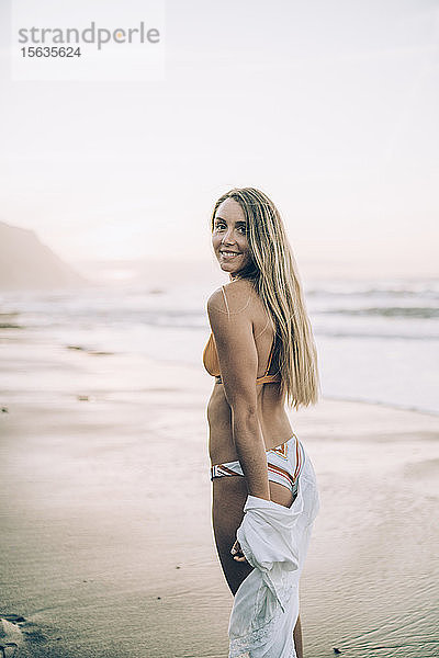 Junge blonde Frau im Bikini am Strand bei Sonnenaufgang