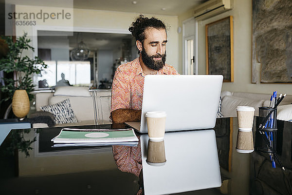 Mann arbeitet zu Hause am Tisch mit Laptop