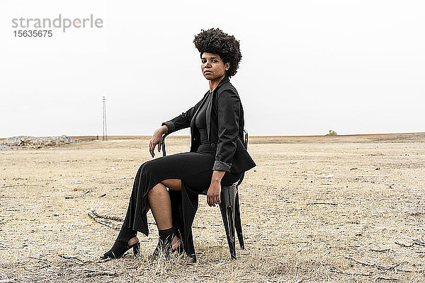 Porträt einer schwarz gekleideten jungen Frau in trostloser Landschaft sitzend