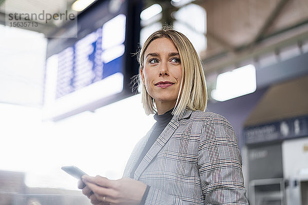 Junge Geschäftsfrau mit Mobiltelefon am Bahnhof