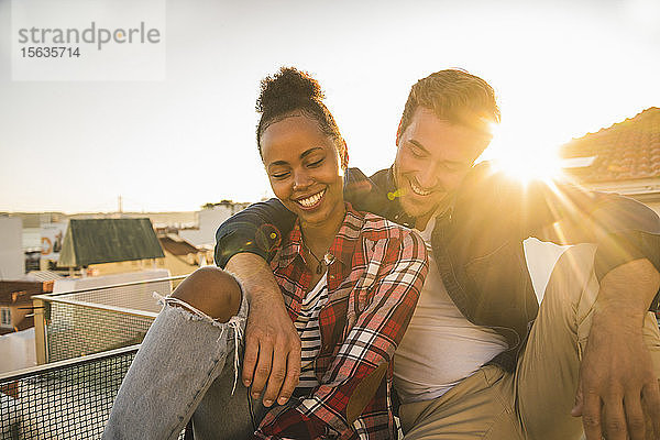 Glückliches  liebevolles junges Paar sitzt bei Sonnenuntergang auf dem Dach