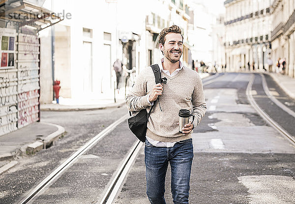 Lächelnder junger Mann mit Rucksack und Kaffeetasse in der Stadt unterwegs  Lissabon  Portugal