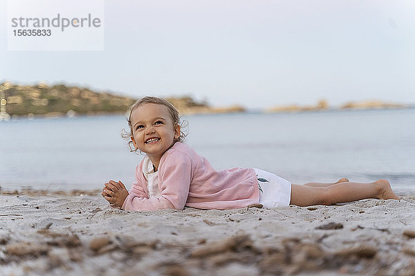 Glückliches süßes Kleinkind am Strand liegend