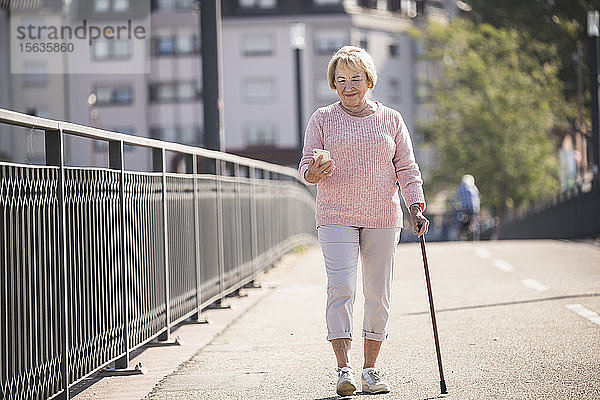 Ältere Frau  die auf einer Fußgängerbrücke geht  mit Gehstock