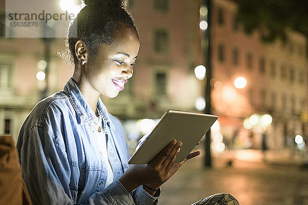 Lächelnde junge Frau mit digitalem Tablet in der Stadt bei Nacht  Lissabon  Portugal