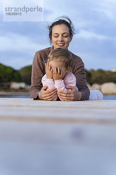 Glückliche Mutter mit Tochter bei Sonnenuntergang auf einem Steg liegend