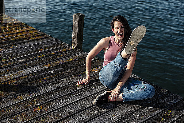 Porträt einer schreienden jungen Frau  die auf einem Steg sitzt und in die Luft tritt  Starnberger See  Deutschland