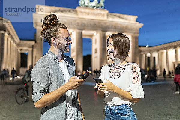 Glückliches Paar benutzt Smartphones am Brandenburger Tor zur blauen Stunde  Berlin  Deutschland