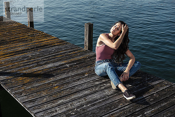 Junge Frau mit geschlossenen Augen beim Relaxen am Steg  Starnberger See  Deutschland