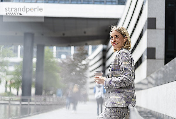 Lächelnde junge Geschäftsfrau mit Kaffee zum Mitnehmen in der Stadt