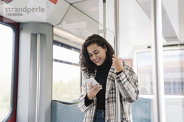 Lächelnde junge Frau mit Smartphone in der U-Bahn