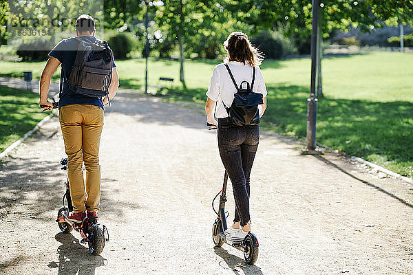 Rückansicht eines Elektroroller fahrenden Paares in einem Stadtpark