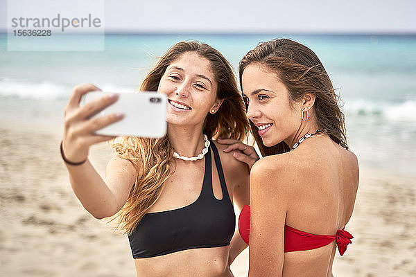 Zwei lächelnde junge Frauen beim Selfie am Strand