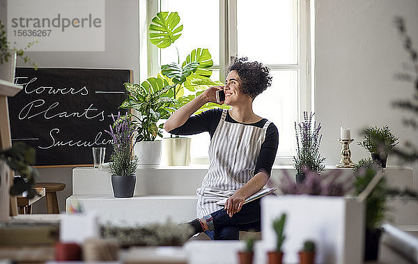 Lächelnde junge Frau am Telefon in einem kleinen Laden mit Pflanzen